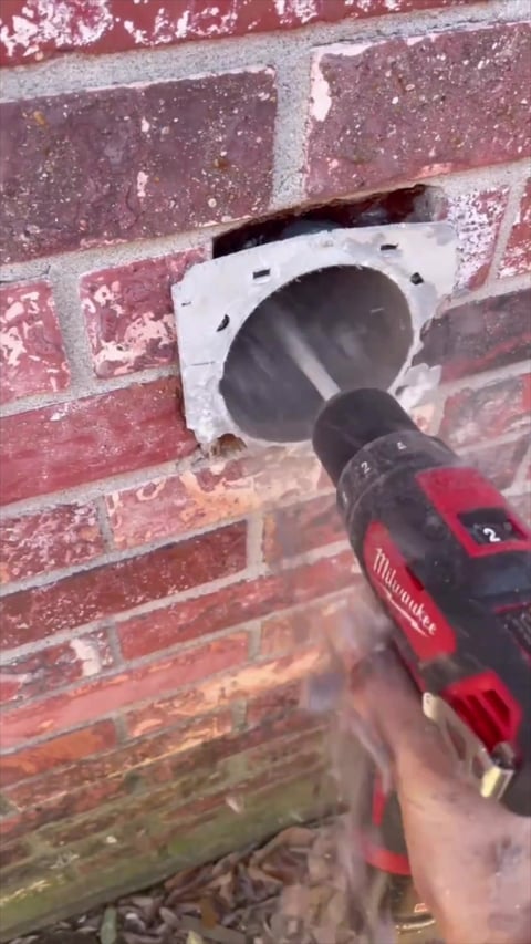 Hand holding Milwaukee drill inserting bit into outlet box on brick wall