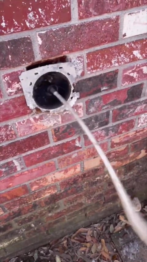 White dryer vent outlet protruding from weathered red brick wall